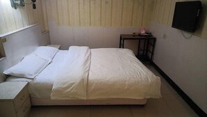 Ein kleines, sauberes Zimmer mit einem Einzelbett, einem Nachttisch, einem kleinen Schrank und einem an der Wand befestigten Fernseher.