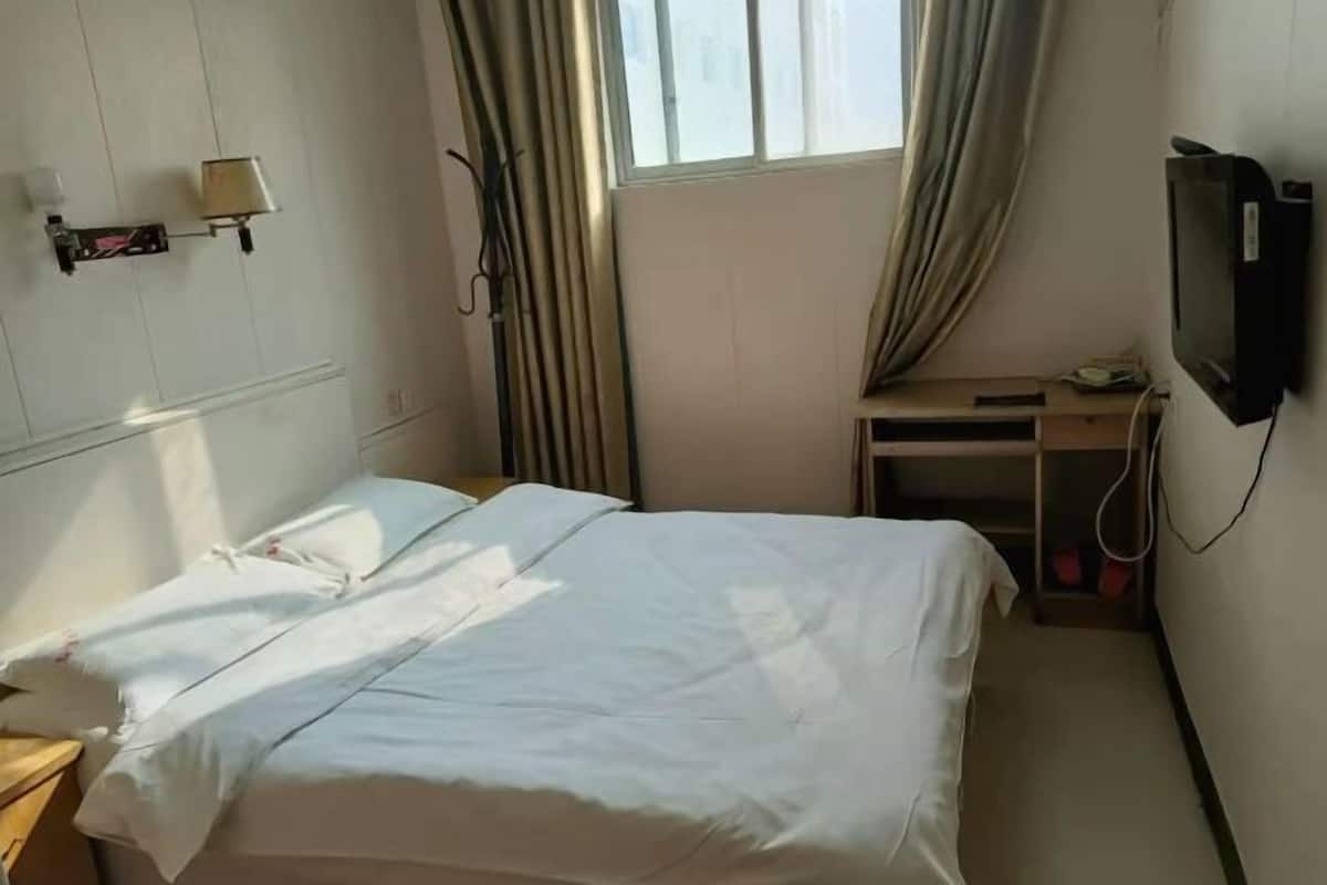 A hotel room with a bed, a desk, a television, and a window with curtains.