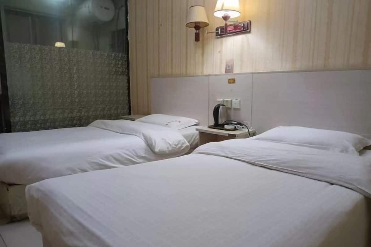 A hotel room with two beds, a nightstand, a lamp, and a window with a curtain.