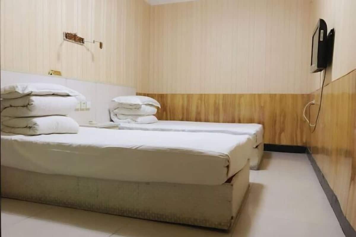 A hotel room with two beds, a wooden wall panel, a wall-mounted phone, and a towel rack.