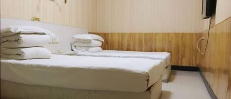 A hotel room with two beds, a wooden wall panel, a wall-mounted phone, and a towel rack.