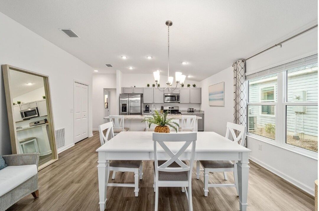 Une cuisine moderne avec des meubles blancs, un îlot central et un coin repas comprenant une table et des chaises blanches.