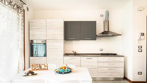A modern kitchen with light wood cabinets, a black range hood, and a gas stove. There is a dining table with white chairs and a decorative crab centerpiece.