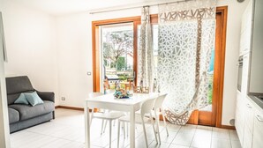 A modern living room with a dining area, a sofa, and a view through a glass door.