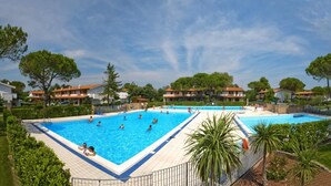 Une grande piscine rectangulaire entourée d’une terrasse carrelée, où plusieurs personnes nagent et se détendent.