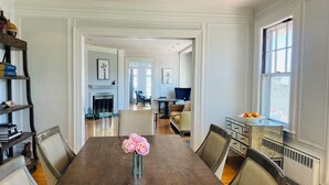 A dining room with a wooden table, chairs, a vase with flowers, and a bookshelf.