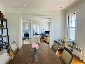 A dining room with a wooden table, chairs, a vase with flowers, and a bookshelf.