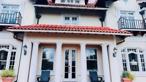 A two-story building with a red-tiled roof, white columns, and a balcony with black railings.