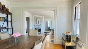 A spacious dining area with a wooden table, chairs, a vase of flowers, and a view into the kitchen.