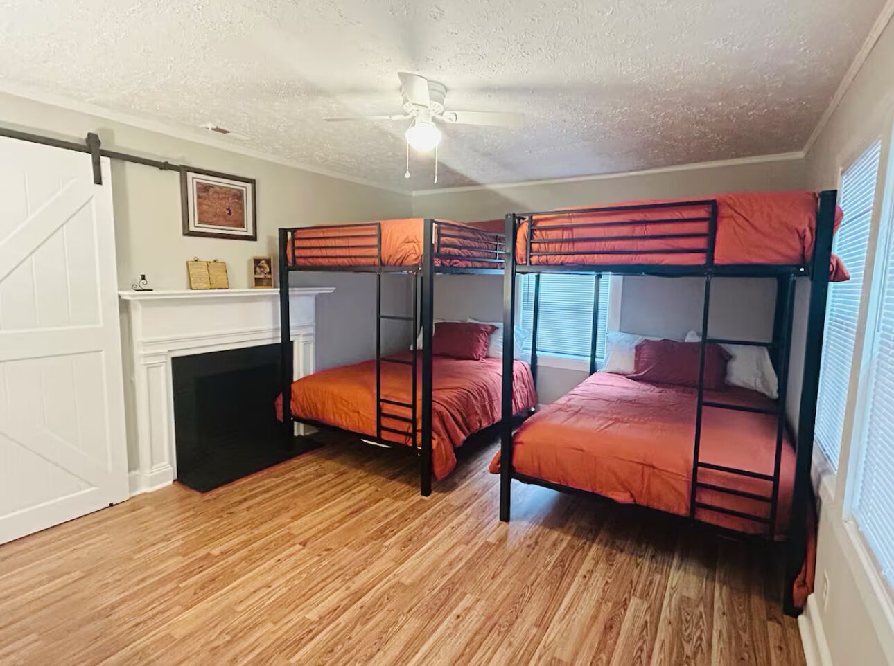 A room with three bunk beds, a ceiling fan, a fireplace, and a window with blinds.