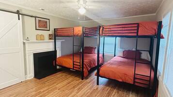 A room with three bunk beds, a ceiling fan, a fireplace, and a window with blinds.
