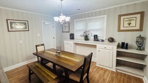 A dining area with a wooden table and benches, a chandelier, and a kitchen with white cabinets and a window. - Rudolph home (Goldsboro)