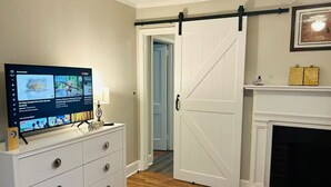 A room with a white dresser, a television displaying a show, a sliding barn door, and a fireplace. - Rudolph home (Goldsboro)