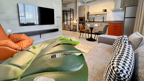 A modern living room with a flat-screen TV, a sofa, and a dining area with chairs and a table. - C Living 2 - Executive - 1BD Apartment City View (Riyadh)