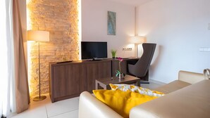 Et moderne hotelværelse med en stenvæg, et fladskærms-tv, et skrivebord med lampe, en stol og en sofa.