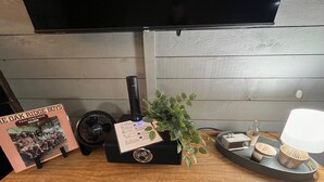 Un escritorio de madera con una radio de estilo antiguo, un ventilador, una planta en maceta, una bandeja con una lámpara y un álbum enmarcado.