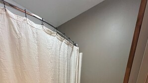 Un baño pequeño con cortina de ducha, inodoro y una cesta de artículos de aseo en la pared.