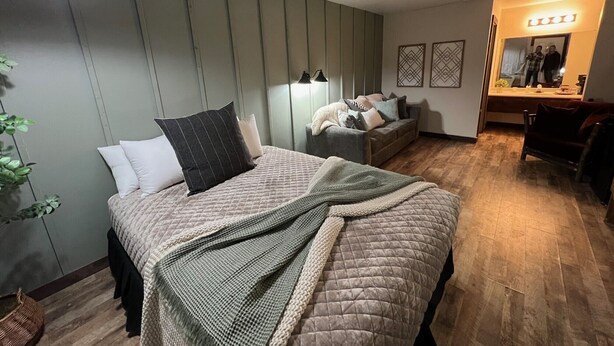 Un dormitorio moderno con una cama, un sofá, un espejo y una planta.