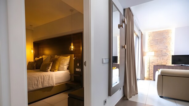 A modern hotel room with a bed, bedside table, lamp, TV, and a view of the outside. - Apartment 'Suite 3' with Shared Pool, Wi-Fi and Air Conditioning (Cala Agulla)