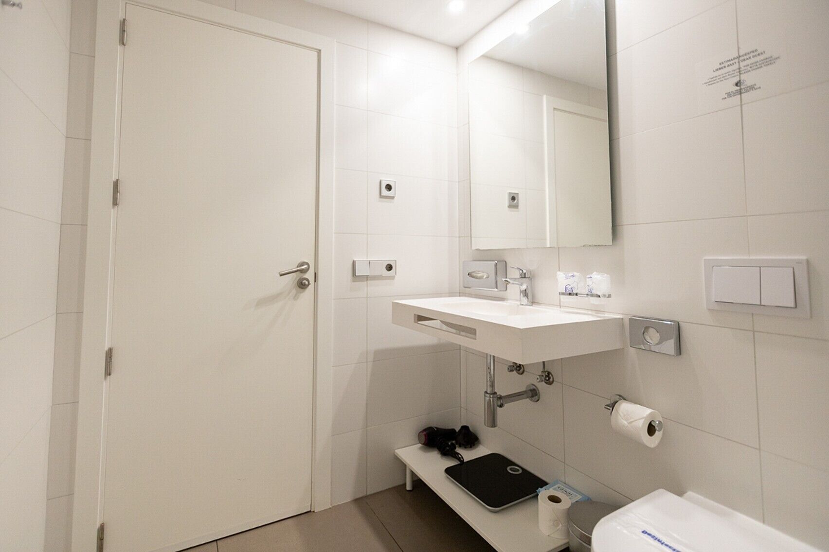 Et moderne badeværelse med hvid vask, spejl og toilet.