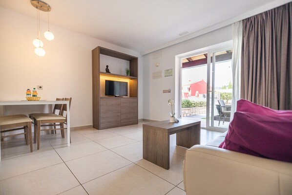 Un salon moderne comprenant un canapé, une table à manger avec des chaises, un téléviseur posé sur un meuble en bois et une porte-fenêtre coulissante donnant sur un espace extérieur.