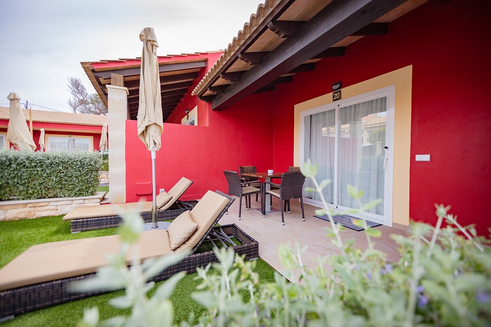 Un bâtiment rouge doté d’un patio comprenant des chaises longues, une table et un parasol.