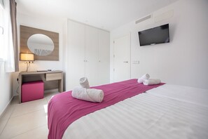 A hotel room with a bed, a desk, a chair, a TV, and a mirror.