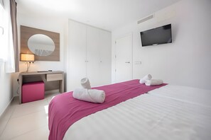 A hotel room with a bed, a desk with a chair, a TV, and a mirror.