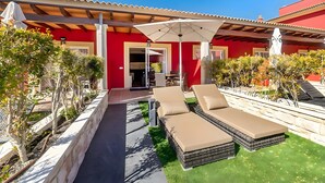 A red building with a covered patio, two lounge chairs, and a table with chairs. - Apartment 'Standard 3' with Shared Pool, Wi-Fi and Air Conditioning (Cala Agulla)