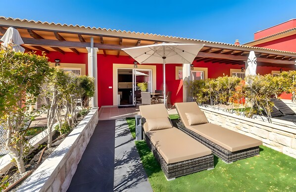 A red building with a covered patio, two lounge chairs, and a table with chairs.