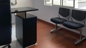 A waiting area with a reception desk, two black chairs, a white door, and a window with a view of buildings outside. - Bogota San Diego Suite, BogotaUrban Suite, BogotaSuite Planetario, turismobogotá (Bogotá)