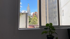 A room with a large window, a potted plant, and a view of a cityscape with buildings and trees. - Bogota San Diego Suite, BogotaUrban Suite, BogotaSuite Planetario, turismobogotá (Bogotá)
