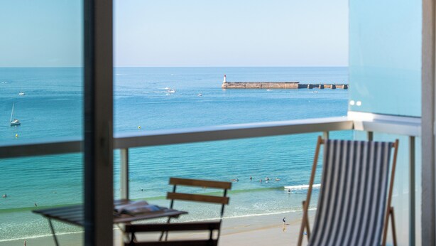 Un balcón con vista al mar, una banca de madera y una silla de playa a rayas.