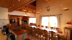 A cozy dining area with a long table, chairs, and a fireplace. - Apartment 'Alpaga 14' with Private Terrace, Shared Garden and Wi-Fi (Bonneval-sur-Arc)