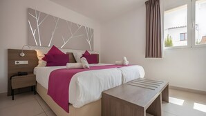 Een slaapkamer met een bed, nachtkastje, lamp en een raam met gordijnen.
