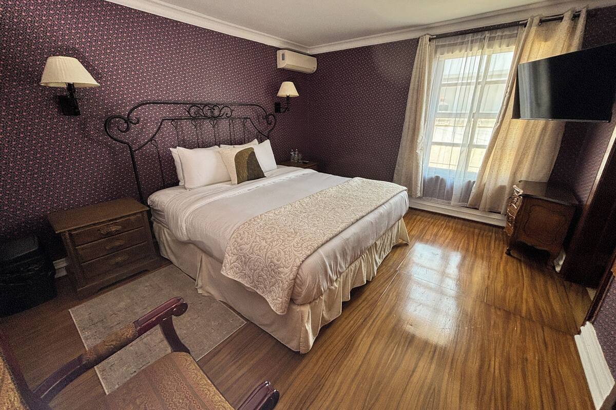 Ein Schlafzimmer mit Bett, Holzboden, Kommode, Nachttisch, Lampe und Fernseher.