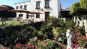 A white building with multiple balconies and a garden with various plants and flowers. - Hacienda San Angel (Ensenada)