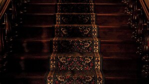 A grand staircase with ornate wooden railings and a patterned carpet. - Hacienda San Angel (Ensenada)