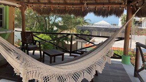 A hammock under a thatched roof structure with wooden furniture and a view of a building in the background.