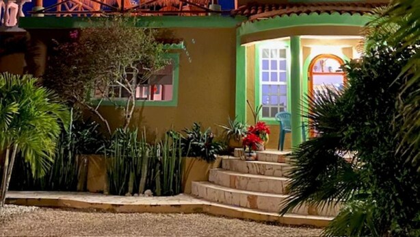 A two-story building with a thatched roof balcony, a green door, and a small porch area with steps.