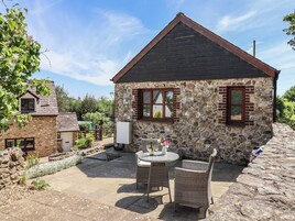 Une maison en pierre avec un toit sombre et un petit porche aménagé avec des meubles en osier.