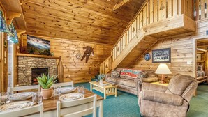 A cozy log cabin interior with a dining area, fireplace, and a staircase leading to an upper level. - King Bed~Hot Tub~Serene setting~Romantic (Sevierville)