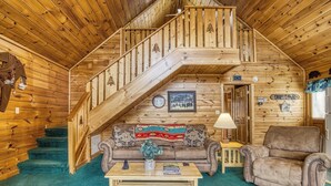 A wooden cabin interior with a staircase, a sofa, a chair, and a coffee table. - King Bed~Hot Tub~Serene setting~Romantic (Sevierville)