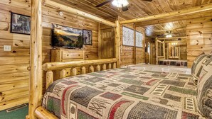 A log cabin room with a large bed, wooden walls, ceiling fans, and framed pictures on the walls. - King Bed~Hot Tub~Serene setting~Romantic (Sevierville)