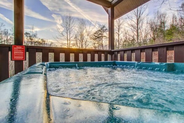 A hot tub under a wooden pergola with a view of trees and a clear sky.
