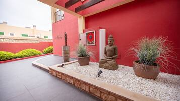 Fachada de un edificio rojo con una estatua de Buda, plantas en macetas y un pequeño jardín.