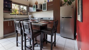 A modern kitchen with dark wooden cabinets, a stainless steel refrigerator, and a dining area with two chairs and a table set for two. - Las Palmas 1BR+Loft w/ Pool—Walk to Beach & Dining (Coco)