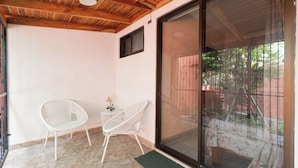 A covered patio with a sliding glass door, a white wicker chair, and a small table with a flower vase. - Las Palmas 1BR+Loft w/ Pool—Walk to Beach & Dining (Coco)