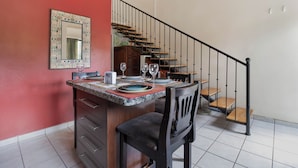 A dining area with a kitchen counter, a chair, and a staircase. - Las Palmas 1BR+Loft w/ Pool—Walk to Beach & Dining (Coco)