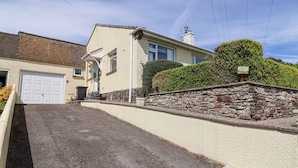 Une maison à deux étages avec un garage, un mur en pierre et un jardin bien entretenu.
